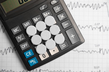 Nine white tablets lie on the buttons of calculator on background of the electrocardiogram. Cardio therapist assistance, physical make cardiac physical. concept of medicine and health care. Calculation of health insurance on calculatorの写真素材