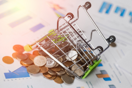 Inverted miniature shopping cart with coins on the office Desk. Symbolic photo for purchasing power and consumption. Finance and money concept mini shopping cart on the table with documentsの写真素材