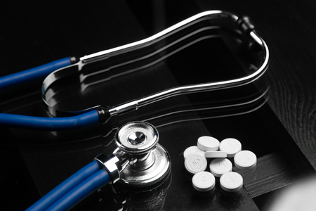 blue stethoscope and a bunch of white pills lie on a black background of a wooden table. Cardio therapist assistance, physical make cardiac physical. concept of medicine and healthの写真素材
