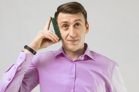 Close-up Portrait of a man in a shirt standing alone in a bright Studio and holding a RAM from the computer. man with a computer part. guy keeps a face memoryの写真素材