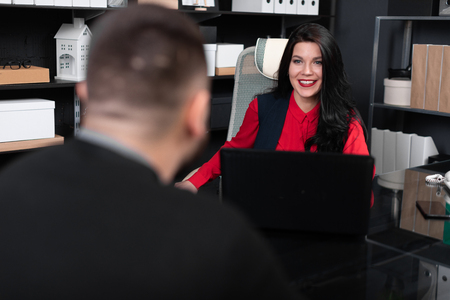 man is interviewed for employment. Dialogue between two young people. Young woman with laptop talking to young man in front of herの写真素材