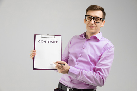 Portrait of a man in a shirt standing alone in a bright Studio and holding a pen and a sheet of contract agreement. Businessman with blank message. Empty Contract agreement in mens handsの写真素材
