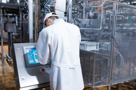 Portrait shot of confident pretty factory worker wearing white coat operating CNC machine at...
