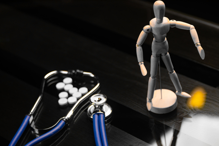 blue stethoscope and a pile of white pills lie next to figure of man on black background of a wooden table. Cardio therapist assistance, physical make cardiac physical. concept of medicineの写真素材