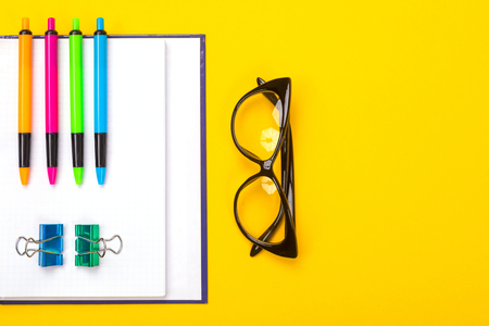 Open diary and four bright handles on it next to the glasses are isolated on the yellow table. Office worker workspace. School supplies for teaching and childrens creativityの写真素材