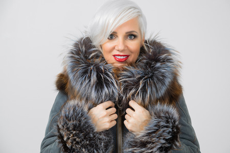 charming blonde in a sheepskin coat with chic fur stands straight and looks at the camera in isolation on a white background. Winter Fashion woman in fur coat, elegant lady portrait. fashion and vogue conceptの写真素材