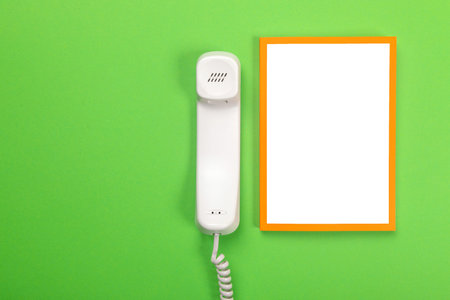 phone with a tube on the table. View from above. Handset on white sheet. A white handset and a blank...
