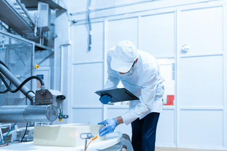 concentrated technologist taking necessary notes with help of digital tablet while standing at production department of dairy factory. The inspector carries out control at the cheese factoryの写真素材