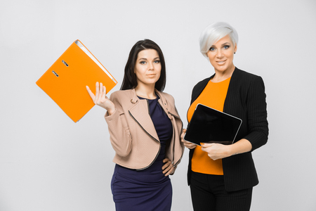 Two attractive smiling women holding folders and tablet against of white background. Isolated, studio shot. portrait of a two young businesswoman discuss with a clipboardの写真素材