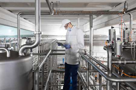 Technologist in a white robe, gloves and mask holding a tablet and stands near the bedon factory...