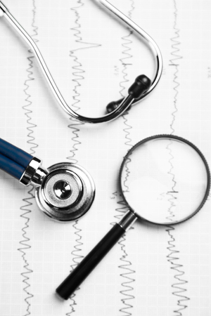 Cardiogram, magnifying glass and blue medical stethoscope. Medical devices on the table at the doctor. concept of medicine and health care. stethoscope head lying on a cardiogram on a clipboard padの写真素材