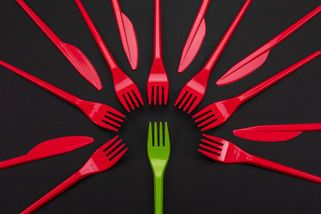 Top view of red and green plastic forks. One green fork surrounded by red forks and knifes