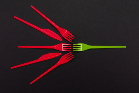 Top view of red and green plastic forks. One green fork surrounded by red forks and knifes