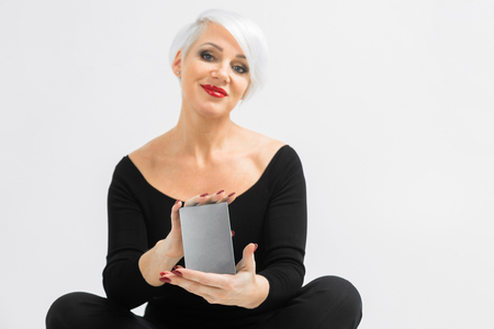 Pretty middle-aged blonde woman smiling with silver box in studio on gray backgroundの写真素材