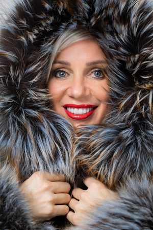 Pretty middle-aged blonde woman smiling with fur in studio on gray backgroundの写真素材