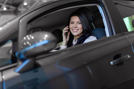 Portrait of smilling happy woman siting in her new vehicle and speaking on smartphone