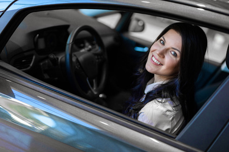 Side view of beautiful happy woman sitting in her new car and examines purchase