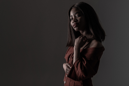 Young beautiful african american girl posing in red sensual dress over dark background. Girl with afro and glamour makeup. Studio shotの写真素材