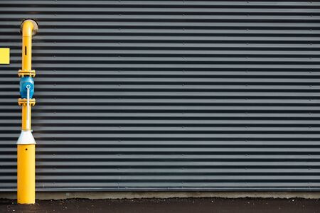 Grey metal grooved wall with yellow pipe