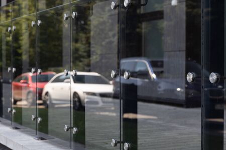 Diagonal view of glass windows or wall with round steel elements with cars and trees reflection on...