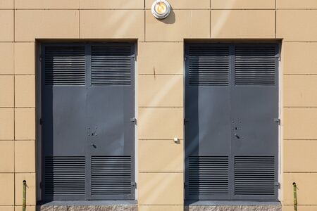 Light beige tiled wall with two grey metal doors and a light in the middle above them