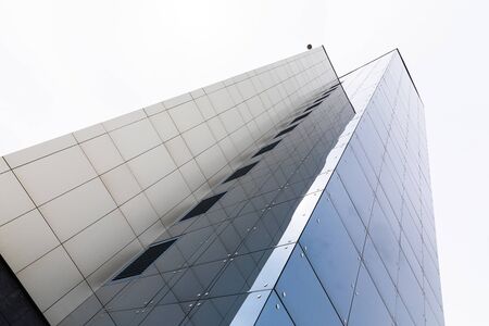 Tall apartment building, ground view. Tiled facade with glass surface