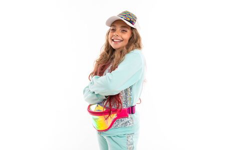 Smiling teenage girl in sparkling clothes, stylish cap and wearing waist bag isolated