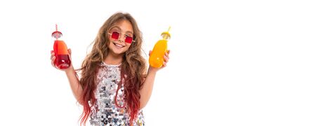 Panorama of girl in sparkling dress and stylish square red sunglasses, holding two glass bottles: with red drink and with yellow drink isolatedの写真素材