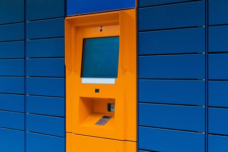 Orange cashpoint minibank with blank copyspace screen on blue panel tile backdrop