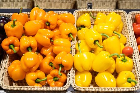 Orange and yellow sweet pepper in baskets on supermarket shelf