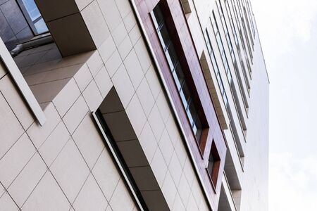 Ground view of tall building facade, fenced with beige square tiles.