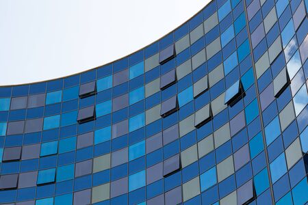 Part of new semicircle bulding with glass walls of blue and golden shades with few windows openedの写真素材