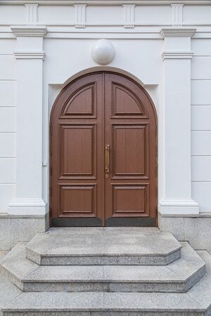 Brown wooden arched door with lamp above it and granite tile stepsの写真素材