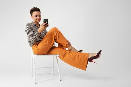 A young beautiful girl sits on a chair with her phone in her hands and thinks.