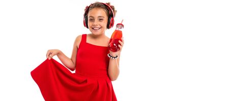 Teenage girl with long blonde hair, dyed tips pink, stuffed in two tufts, in red dress, with red headphones, bracelet, standing and holding phone in hand and drinks juice in glass bottle with a tube.の写真素材