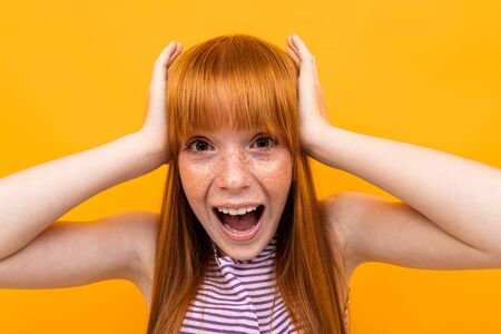 red-haired girl grabbed her head in surprise on an orange backgroundの写真素材