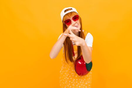 pretty schoolgirl grimaces on an orange background, looks at the camera with a grimace on her face