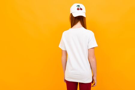 red-haired teenager stands with his back to the camera on a yellow isolated background