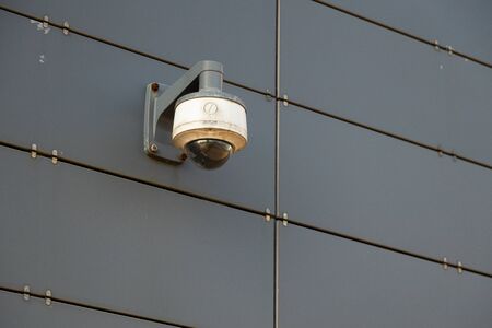 One white-grey surveillance camera on red metal wall. Photo with depth of fieldの写真素材