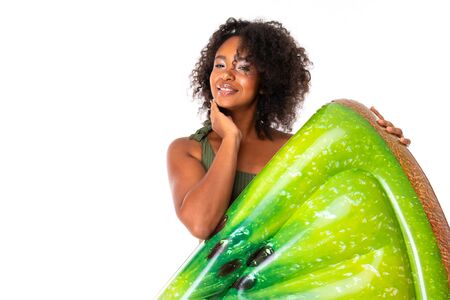 Pretty african female stands in swimsuit with rubber beach kiwi mattress and smiles isolated on white background.の写真素材