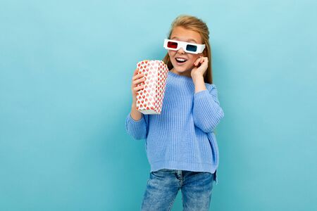 beautiful excited schoolgirl with popcorn and glasses for 3D movie on a blue background