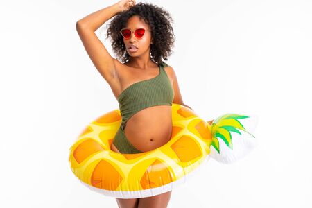 Pretty african female in swimsuit stands with big colourful rubber ring and dancing and smiles...