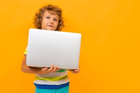Red-haired curly boy with a laptop on a yellow background.