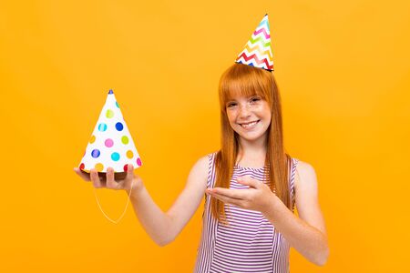 red-haired girl with a holiday cap smiles at the camera on a yellow background.