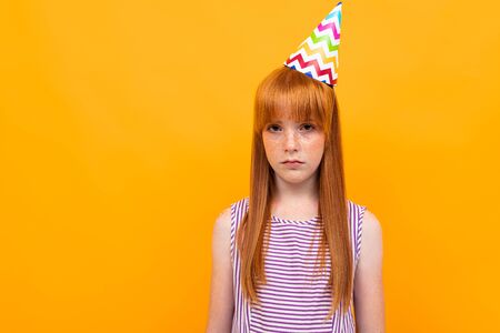 red-haired girl with a holiday cap looks at the camera on a yellow background.の写真素材