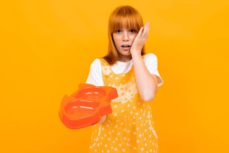 red-haired girl holding an empty pet food bowl on a yellow background.の写真素材