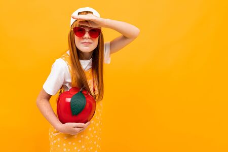 smiling girl in glasses and with a red handbag in the shape of an apple is grimacing at the camera on a yellow background.の写真素材