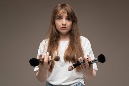 Caucasian teenager do makeup with brushes and is confused isolated on brown background.の写真素材