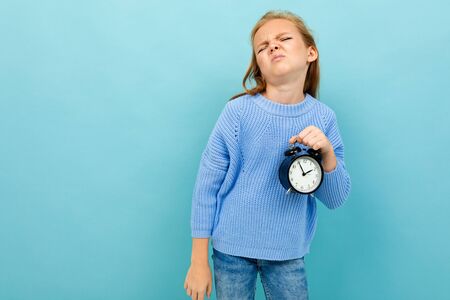 european girl holding an alarm clock on a light blue background.