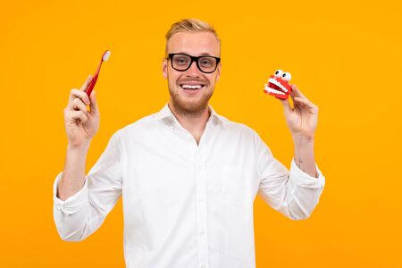 European guy in glasses and a white dress shirt holds a baby brush on a yellow background